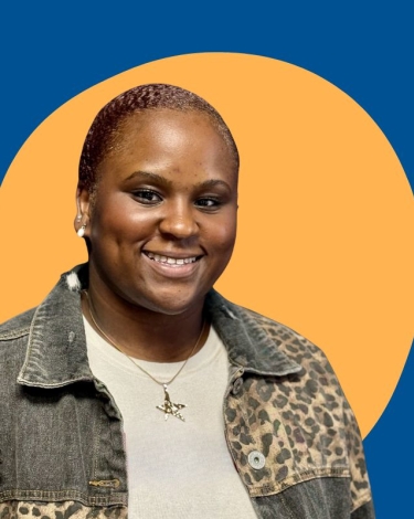 A person wearing a denim jacket with leopard print accents and a star pendant necklace, smiling at the camera.